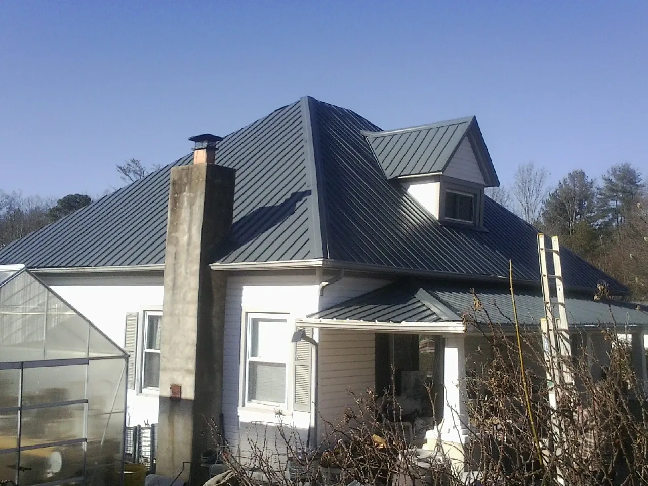 Dark blue standing seam metal roof on a white farmhouse with dormer — Slate & Tile Roof Repair by Roofing Brothers in Swan