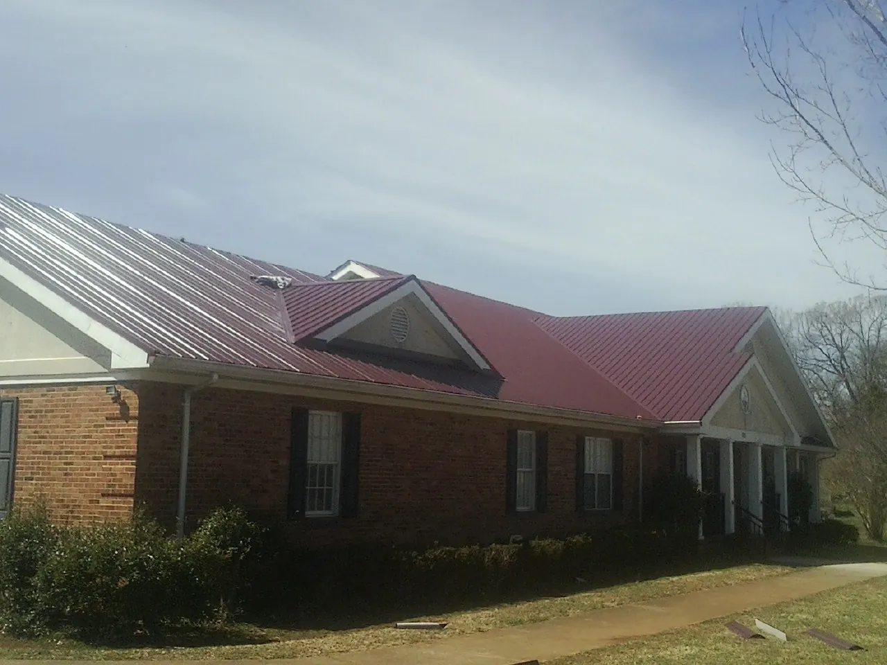 Red metal roof with gabled entries on a long brick building, from a Hail Damage Roof Repair job in Swan