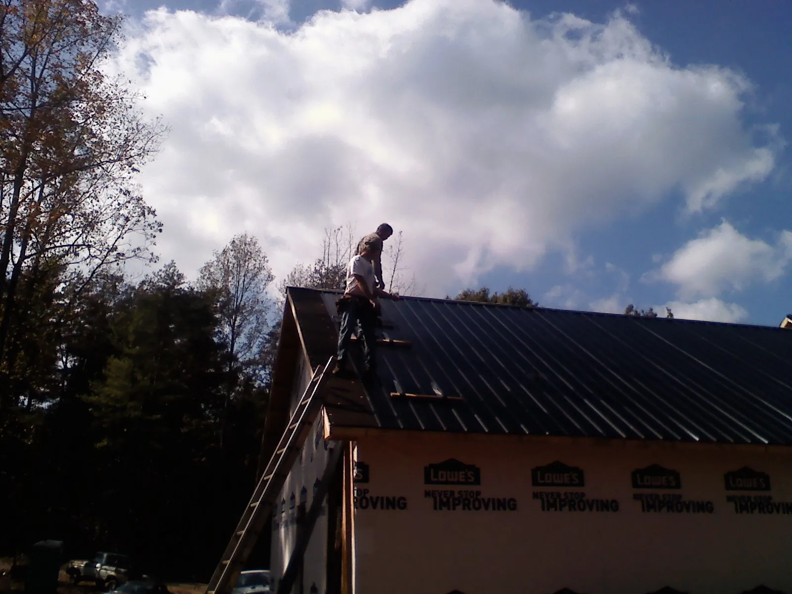 Roofer fastening dark metal panels high against a cloudy sky, from a Roof Inspection job in Swan