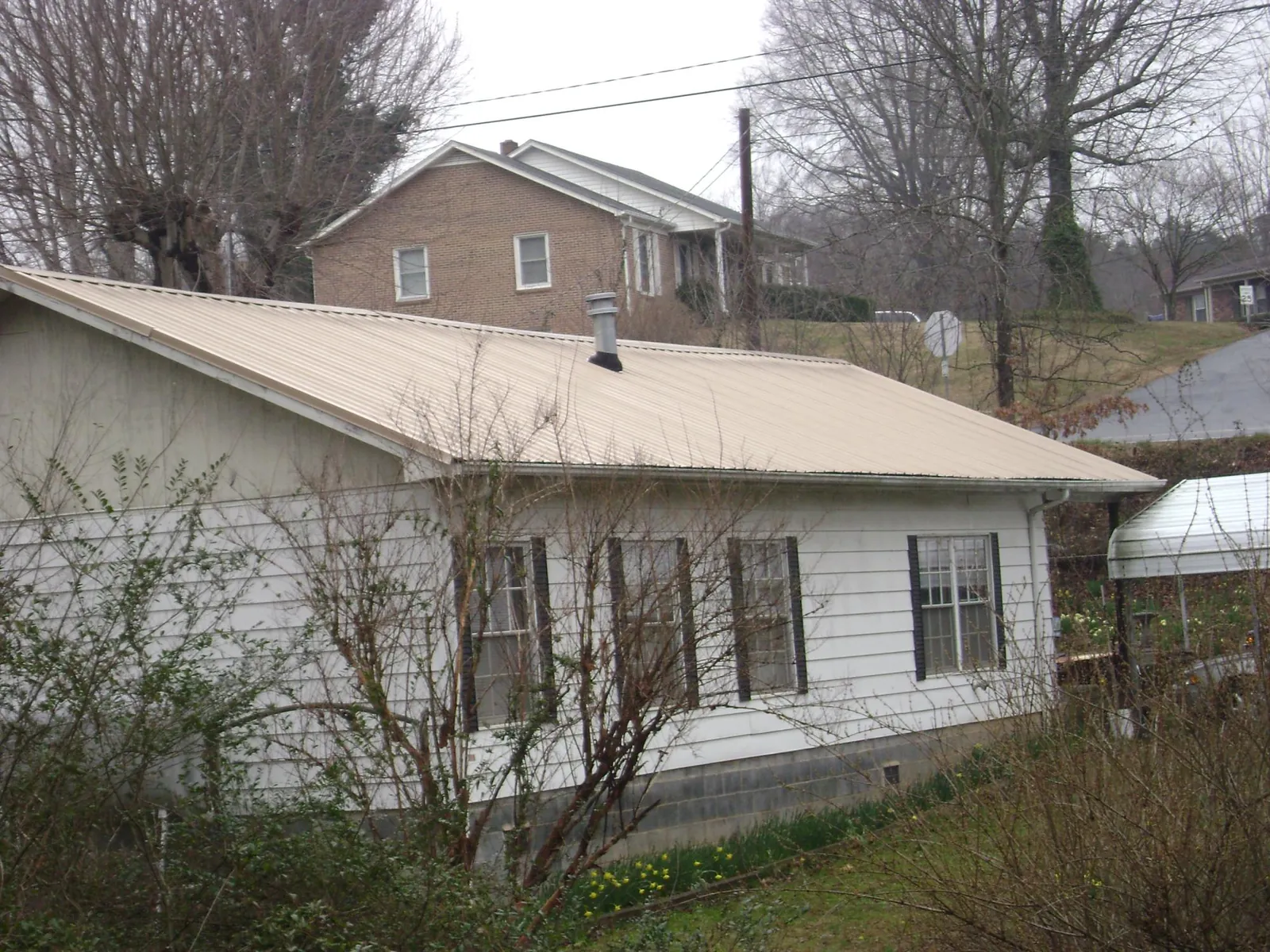 Tan metal roof on a white sided house set into a hillside — Commercial Roofing by Roofing Brothers in Swan